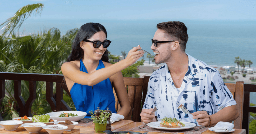 Couple enjoying an outdoor dining experience with a view of the ocean at Cove Rotana Resort, Ras Al Khaimah.