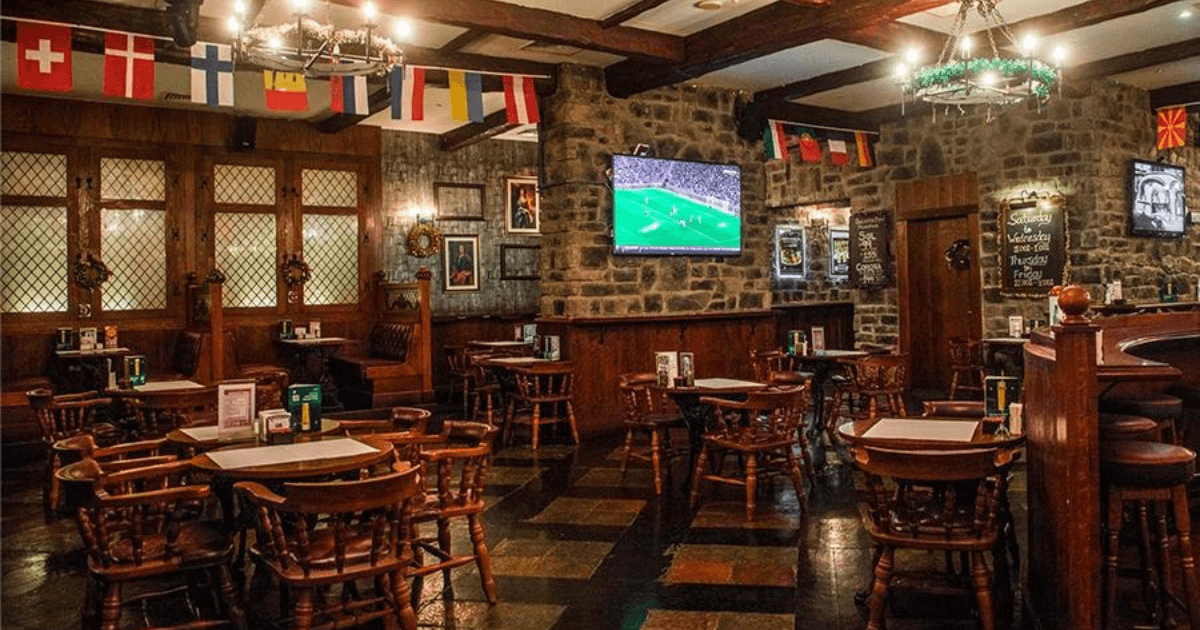 The cozy interior of Nell Gwynne sports bar, with wooden tables and chairs, large TV screens broadcasting a football match, and flags from various countries hanging from the ceiling, creating a welcoming and international ambiance.